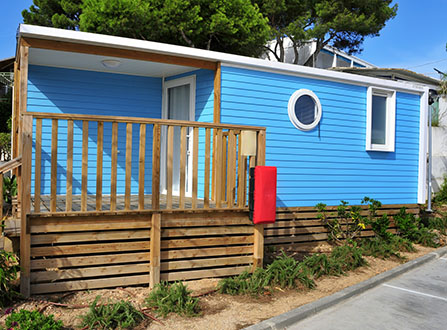 a nice blue mobile home with a wooden veranda in a campsite